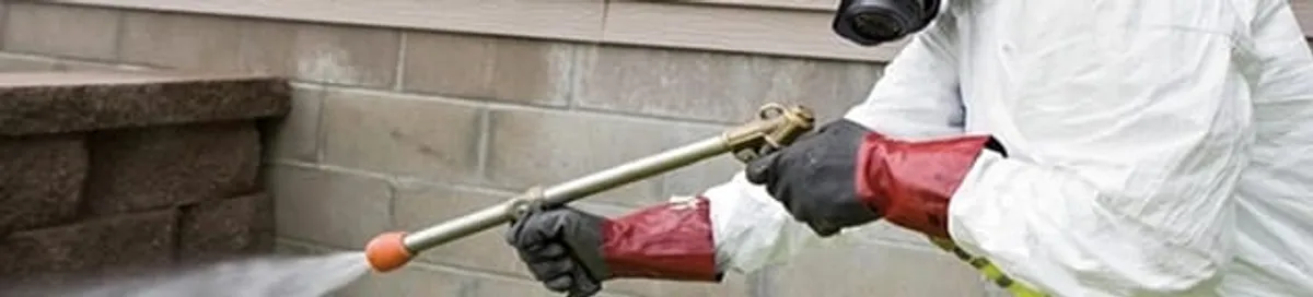 Pest control technician applying exterior insect treatment along a home foundation in Hollywood, FL