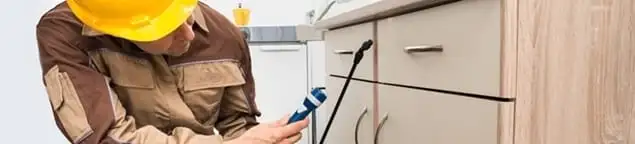 Roach exterminator applying treatment under kitchen cabinets in Hollywood, FL