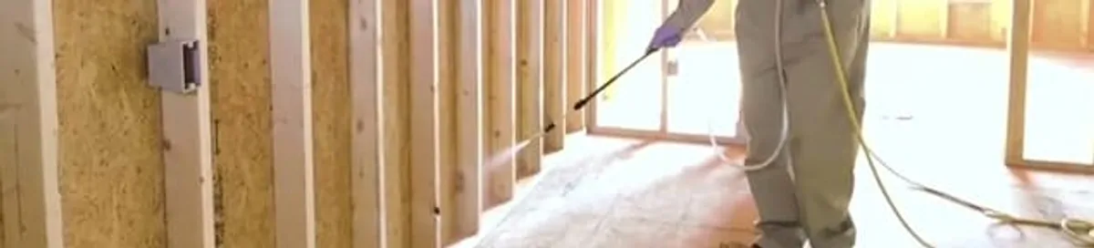 Termite treatment technician applying spray along framing and unfinished walls in Hollywood, FL