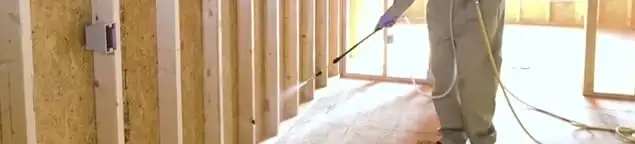 Termite treatment technician applying spray along framing and unfinished walls in Hollywood, FL